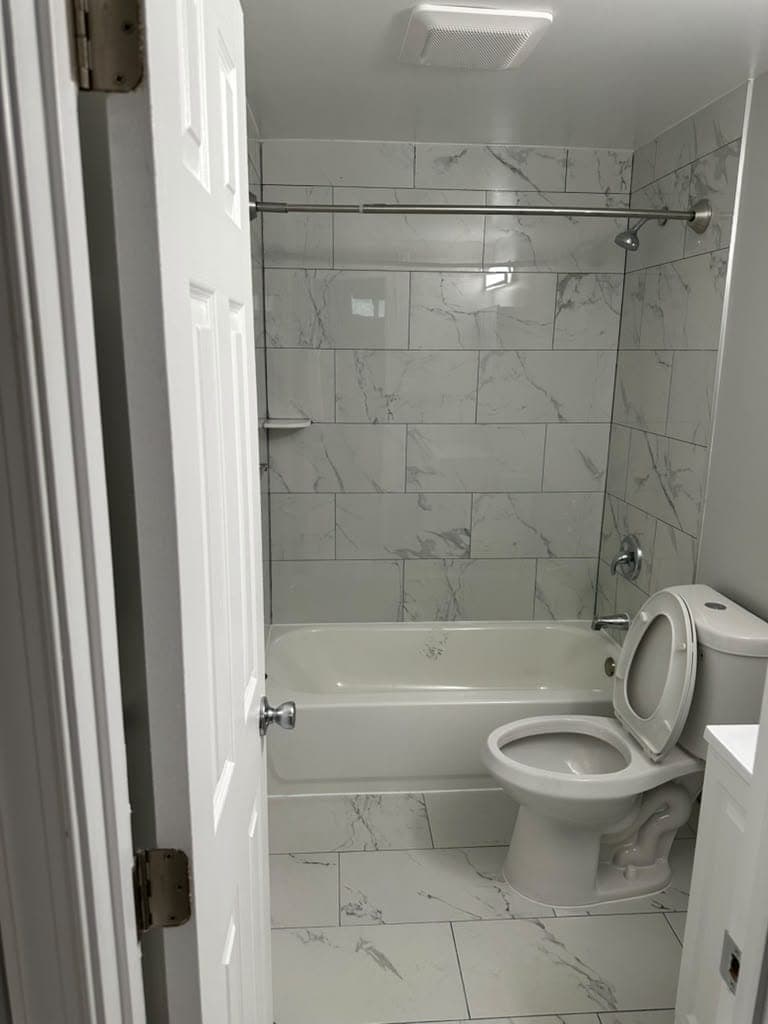 Remodeled bathroom with marble-look tile tub surround and tile floor